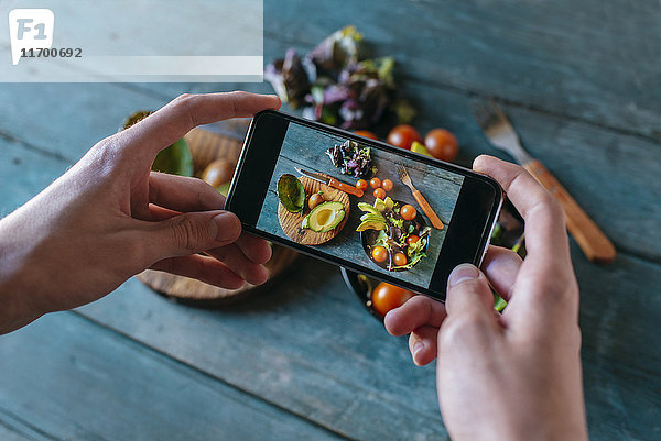 Nahaufnahme der Männerhände beim Fotografieren von Avocadosalat mit Smartphone