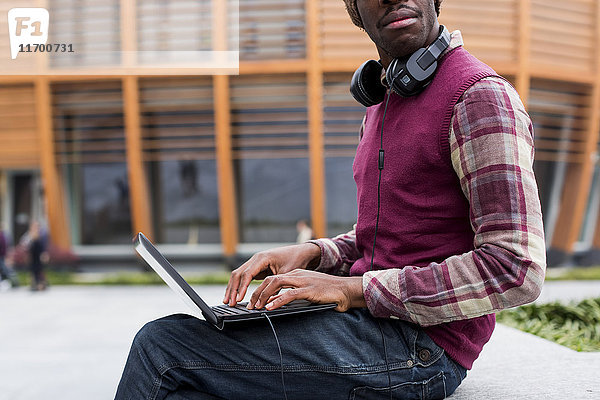 Mann mit Kopfhörer auf der Bank sitzend mit Laptop  Teilansicht