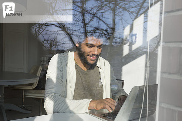 Mann arbeitet am Fenster zu Hause mit Laptop