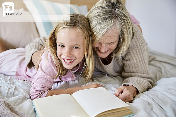 Porträt eines glücklichen kleinen Mädchens  das mit seiner Großmutter auf dem Bett liegt.