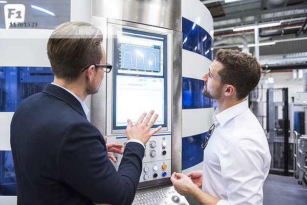 Zwei Männer  die in der Fabrikhalle reden und auf den Bildschirm schauen.