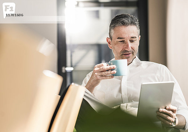 Portrait eines Geschäftsmannes mit Tasse Kaffee in seinem Büro mit Tablette