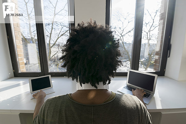 Mann arbeitet zu Hause vor dem Panoramafenster mit Laptop und Tablett