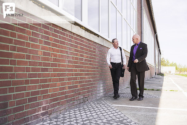 Zwei Männer  die am Fabrikgebäude entlanggehen und reden.