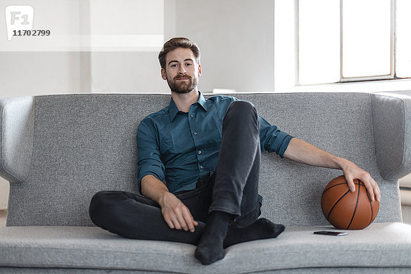 Porträt eines entspannten jungen Mannes auf der Couch mit Basketball