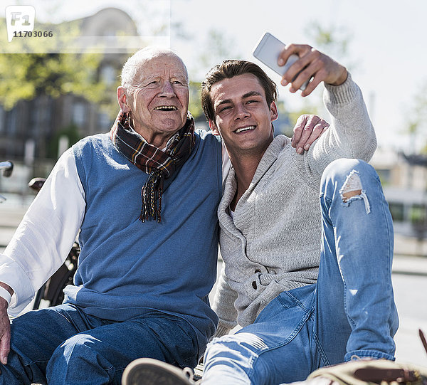 Senior-Mann und erwachsener Enkel auf einer Bank mit einem Selfie