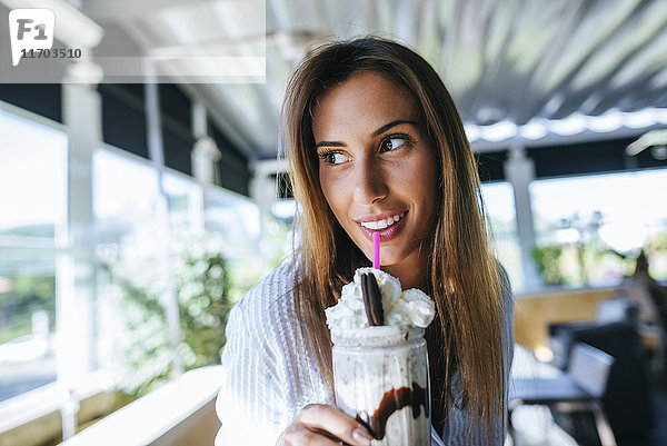 Porträt einer lächelnden Frau beim Trinken von Schokoladen-Milchshake auf der Terrasse