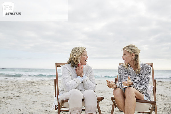 Mutter und Tochter sprechen am Strand und sitzen in Liegestühlen.