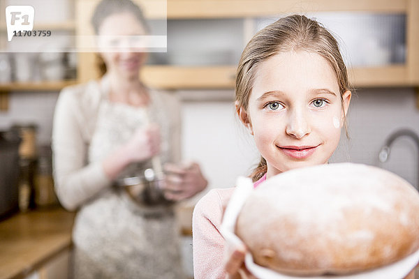 Mädchen mit Brot in der Küche mit Mutter im Hintergrund