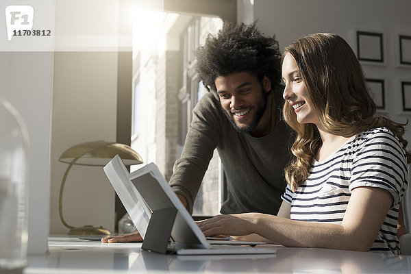 Lächelndes Paar arbeitet zu Hause mit Laptop und Tablett