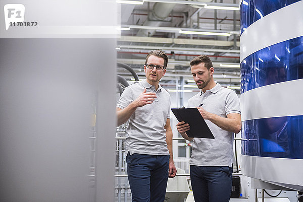 Zwei Männer reden an der Maschine in der Fabrikhalle.