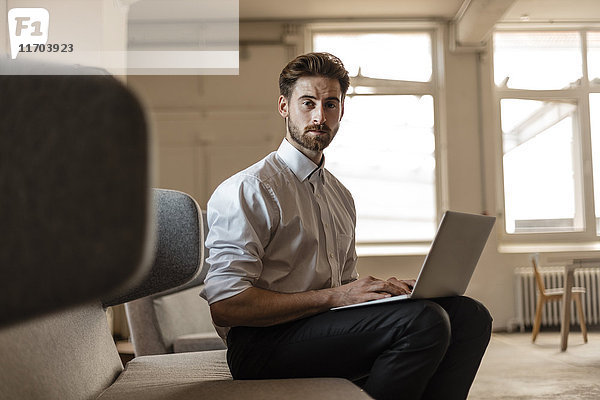 Portrait eines jungen Geschäftsmannes mit Laptop im Loft