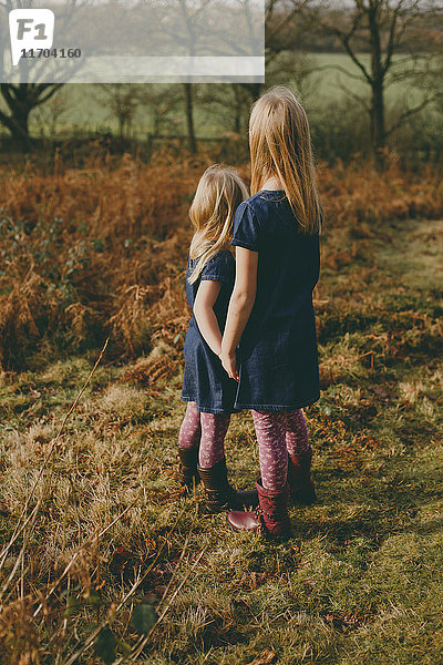 Zwei Schwestern  die auf einer Wiese stehen und Händchen halten.
