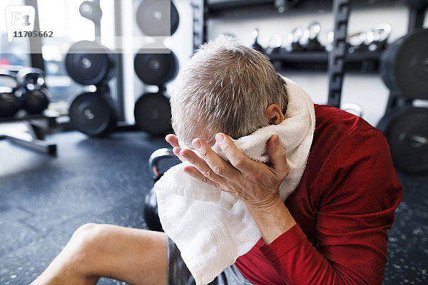 Erschöpfter älterer Mann  der nach dem Training im Fitnessstudio auf dem Boden sitzt.