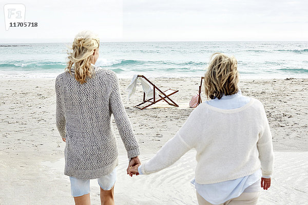 Mutter und Tochter gehen am Strand und halten sich an den Händen.