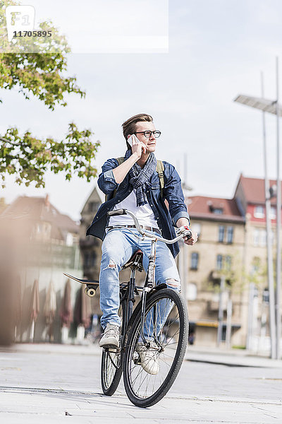 Junger Mann mit Fahrrad in der Stadt telefoniert mit dem Handy