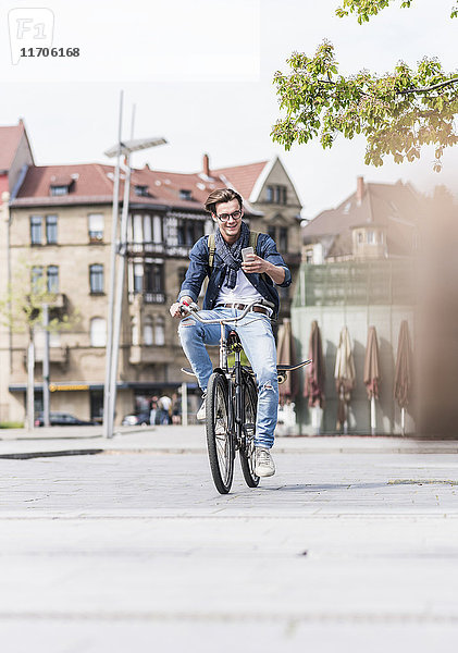 Lächelnder junger Mann mit Fahrrad in der Stadt mit Blick auf Handy