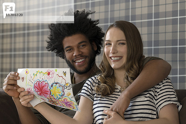 Lächelndes Paar auf der Couch sitzend mit Kinderzeichnung