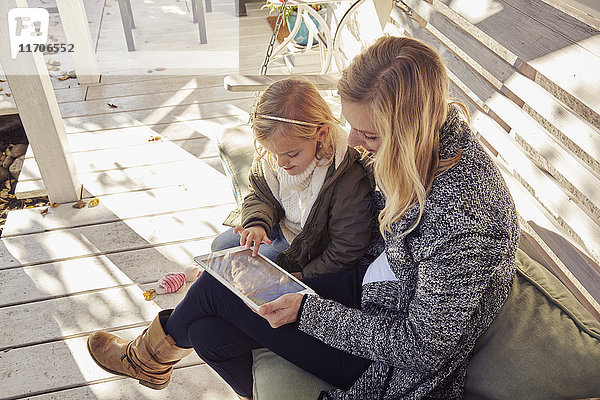 Mutter mit Tochter auf Bank mit Tablette