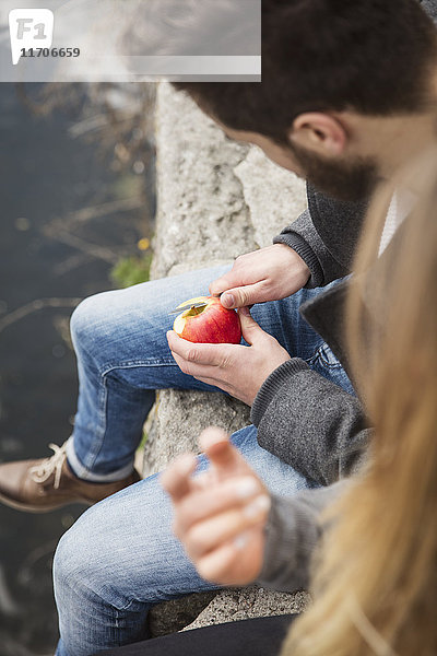 Paar auf Wand sitzend  Apfel schälend