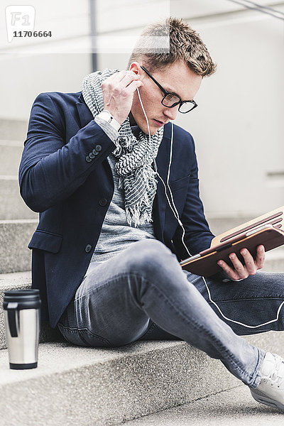 Ein junger Geschäftsmann sitzt auf einer Treppe und benutzt ein digitales Tablett.