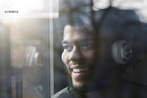 Mann am Fenster mit Blick nach draußen und Musik hören mit Kopfhörern