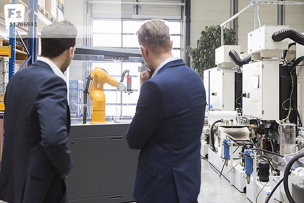 Zwei Geschäftsleute in der Fabrikhalle mit Blick auf Industrieroboter