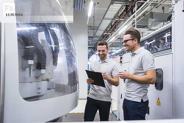 Zwei lächelnde Männer reden an der Maschine in der Fabrikhalle.