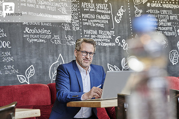 Portrait eines selbstbewussten reifen Geschäftsmannes im Cafe mit Laptop