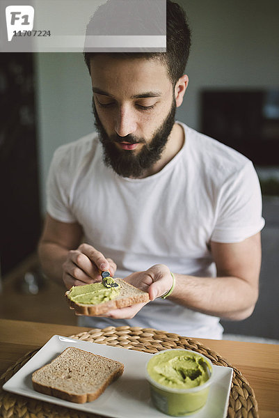 Junger Mann beim Frühstück zu Hause  Toast mit Avocadocreme