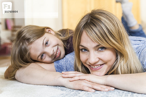 Porträt einer lächelnden  blonden Frau  die mit ihrer Tochter auf dem Boden liegt.