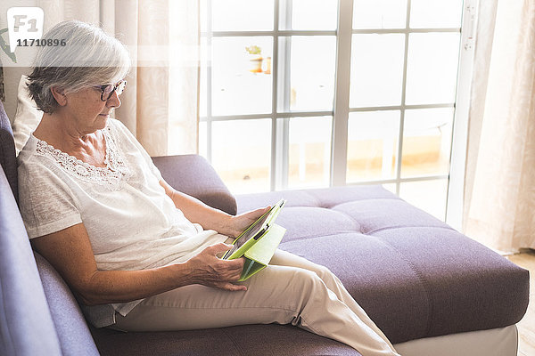 Seniorin auf der Couch sitzend mit Tablette