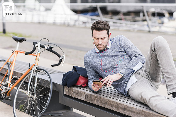 Geschäftsmann in der Stadt mit Fahrrad über Smartphone und Kopfhörer