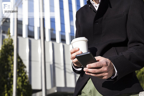 Mann mit Smartphone und Kaffee zum Mitnehmen  Teilansicht