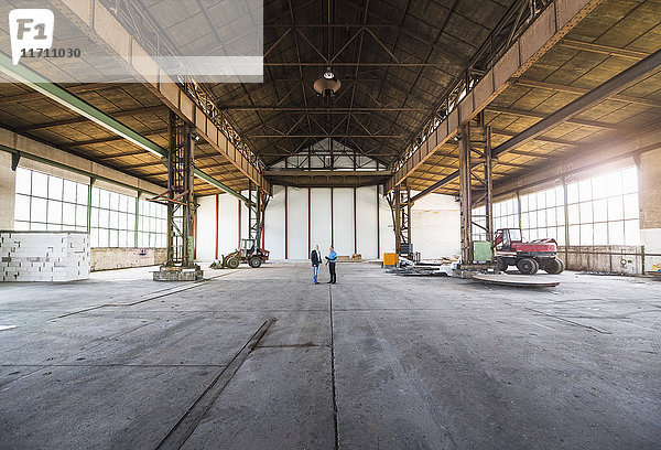 Zwei Geschäftsleute mit Dokumenten  die in der alten Industriehalle reden.