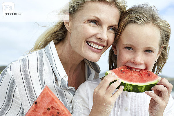 Mutter und Tochter essen Wassermelone am Strand
