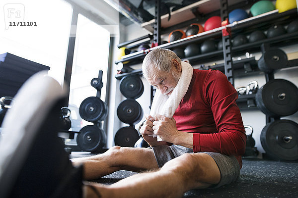 Erschöpfter älterer Mann  der nach dem Training im Fitnessstudio auf dem Boden sitzt.