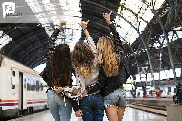 Rückansicht von drei jungen Frauen  die Arm in Arm auf Plattform stehen.