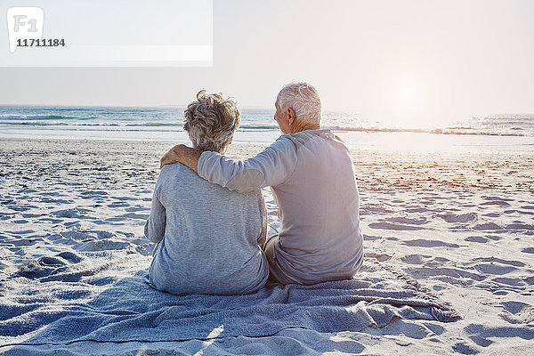 Seniorenpaar sitzt am Strand und schaut in die Ferne.