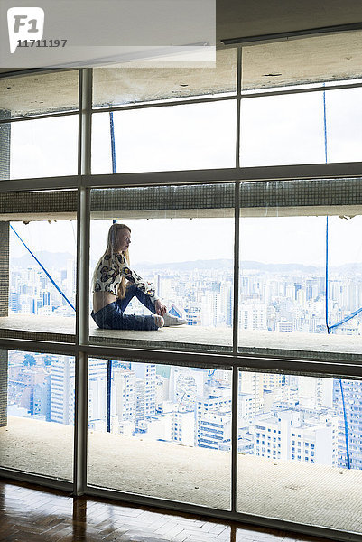 Junge Frau im Hochhaus sitzend im Fenster  Blick über die Stadt