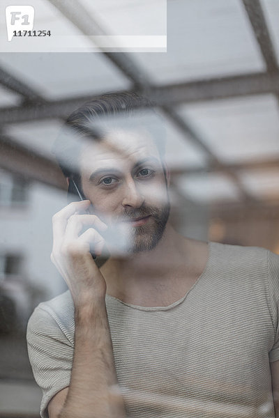 Porträt eines jungen Mannes am Telefon hinter der Fensterscheibe