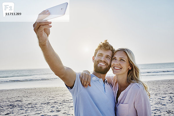 Ein glückliches Paar mit einem Selfie am Strand