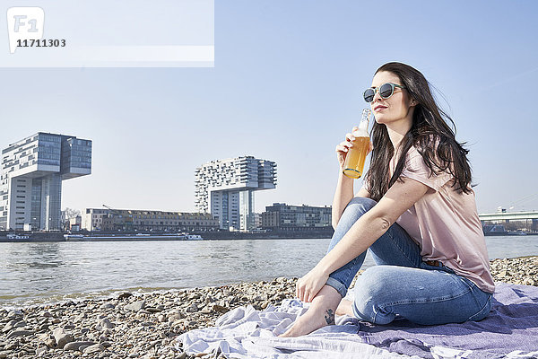 Deutschland  Köln  junge Frau entspannt und bei einem Bier am Rhein