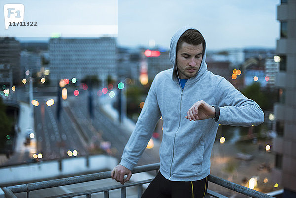 Athlet  der im Morgengrauen seine Smartwatch über der Stadt überprüft.