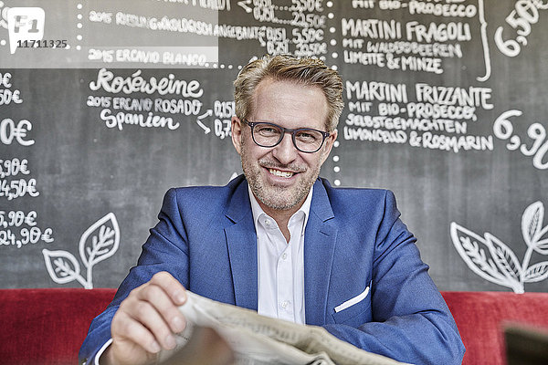 Porträt eines lächelnden reifen Geschäftsmannes im Café beim Zeitungslesen