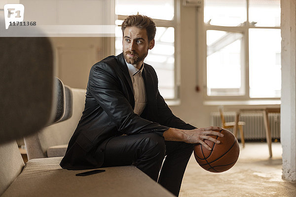 Porträt eines jungen Geschäftsmannes mit Basketball auf der Couch im Dachgeschoss