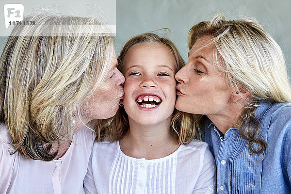 Porträt des glücklichen kleinen Mädchens von Mutter und Großmutter geküsst