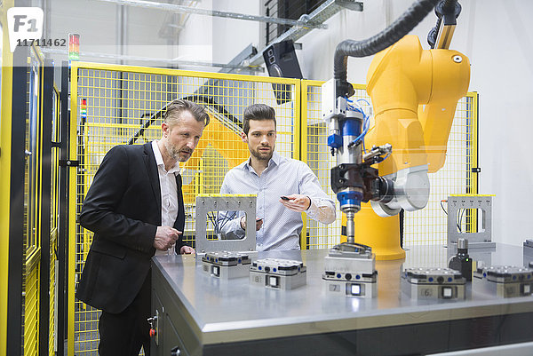 Zwei Geschäftsleute beobachten Industrieroboter in der Fabrik