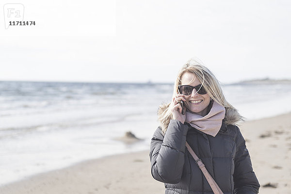 Porträt der glücklichen Frau am Telefon am Strand
