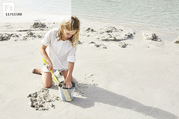Kleines Mädchen spielt am Strand mit Eimer und Schaufel